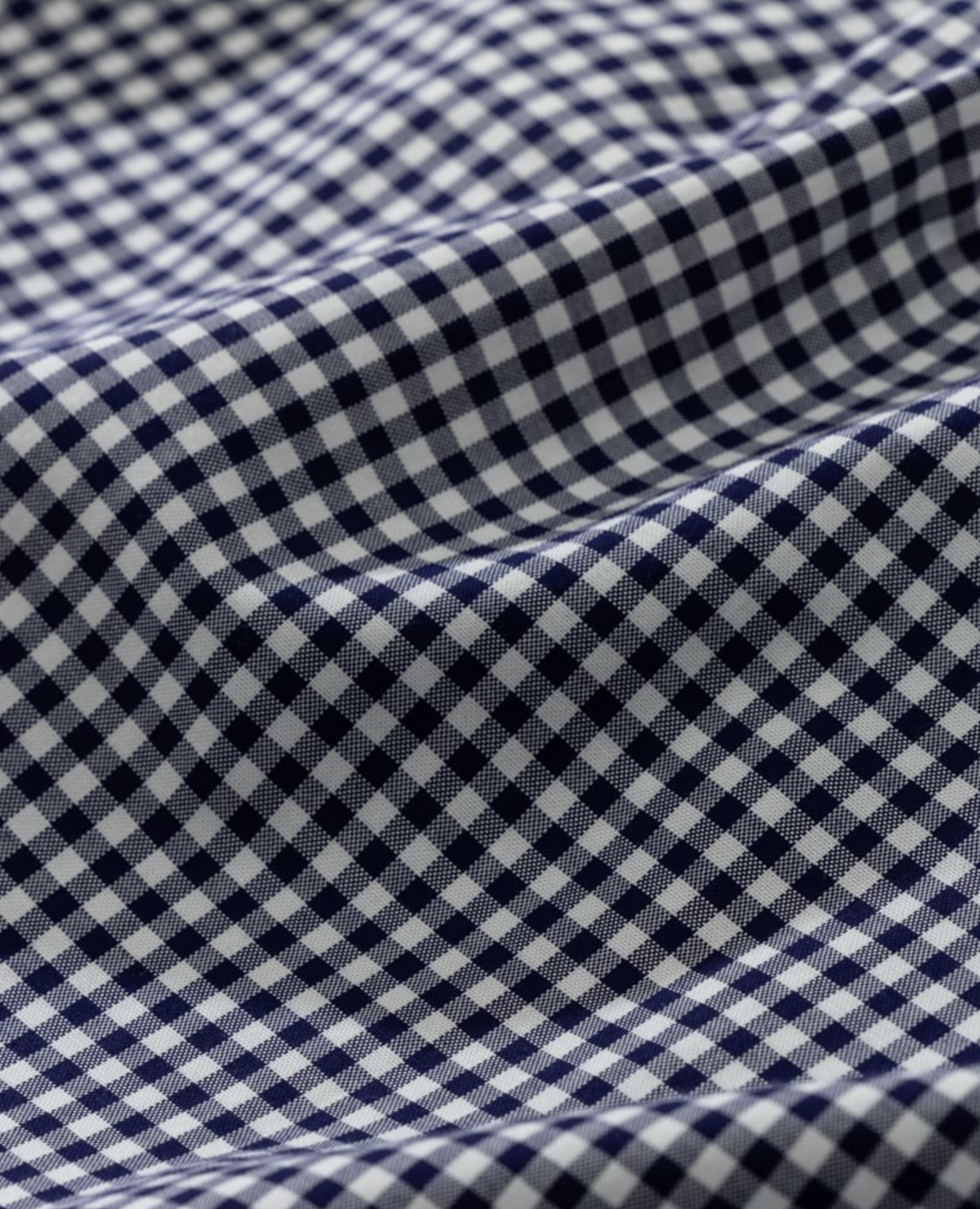A close-up of the 100% cotton blue and white gingham fabric with a small check pattern reminiscent of a classic Rodd & Gunn Superfine Gunn Check Oxford Sports Fit Shirt, creating gentle waves and shadows that highlight its texture.
