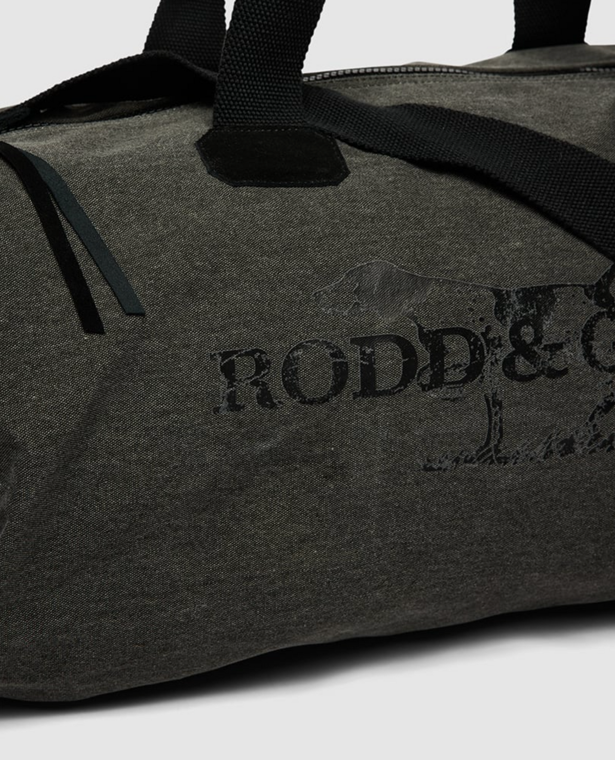 A close-up of the Rodd & Gunn Double Barrel Duffle Bag in dark grey cotton canvas with black handles, featuring a faded logo and partial dog image on its textured fabric.