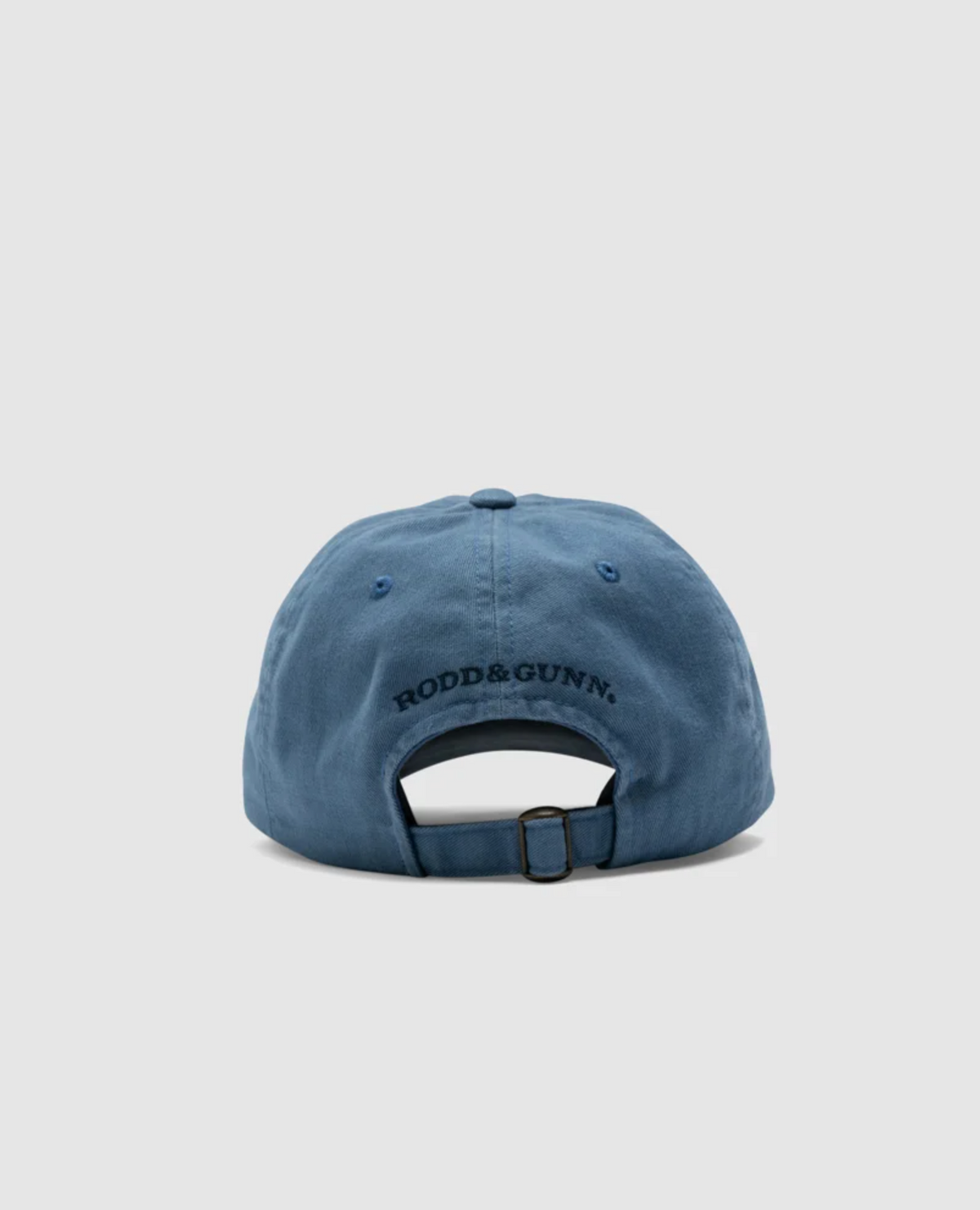 The Rodd & Gunn Signature Cap, made of blue cotton twill, is shown from the back against a light gray background. The cap displays "RODD & GUNN" branding in black text and features an adjustable strap with a metal buckle.