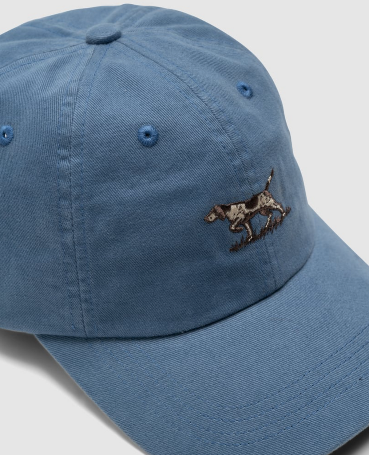 The Rodd & Gunn Signature Cap is a blue cotton twill baseball cap featuring an embroidered dog design on the front. It includes a curved brim, visible stitching, ventilation holes, and an adjustable strap for the perfect fit.