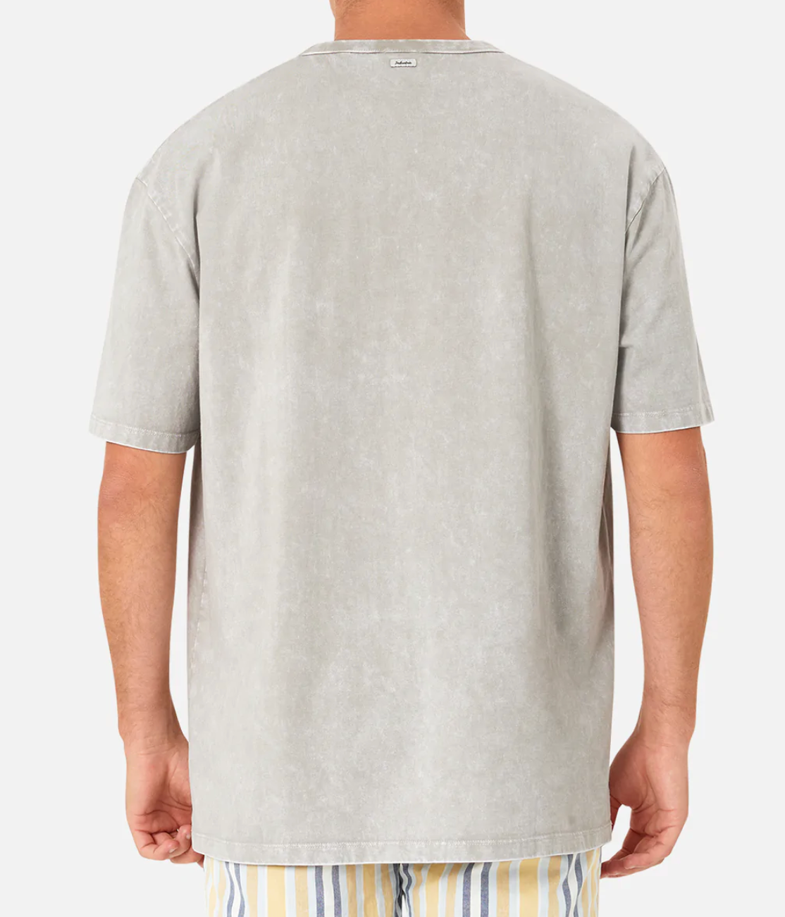 The image shows a person from the back wearing the Industrie The Del Sur Acid Wash Tee featuring a small label at the neckline, paired with light-colored shorts with blue, yellow, and white vertical stripes.