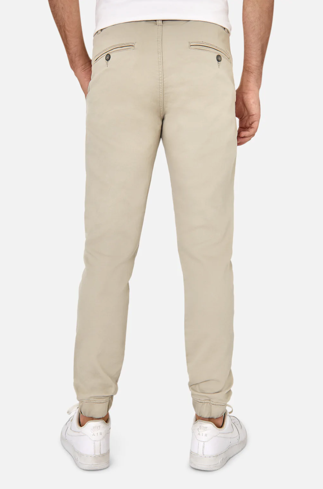 A person is shown from the back wearing Industrie The Drifter Chino Pant, slim fit in beige, and white worn-in sneakers on a plain white background. The chinos feature two buttoned back pockets, while the sneakers add a casual touch.