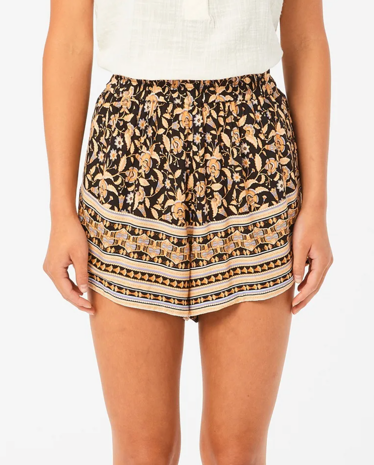 A person wearing Rip Curl Dreamer Short, featuring a black floral pattern with orange and cream details, paired with a white top. The EcoVero/Viscose blend outfit pops against a plain background.