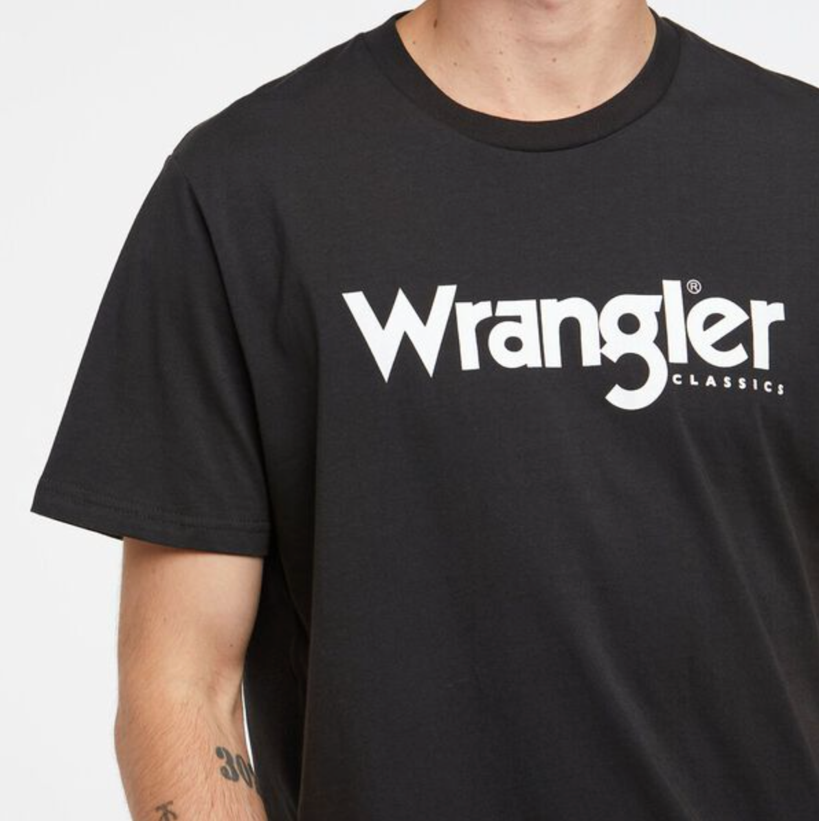Someone is wearing the Wrangler Classic Logo Tee, boasting "Wrangler" in bold white on black, with "Classics" subtly noted for timeless appeal. Made from 100% cotton, this T-shirt ensures ultimate comfort and style.