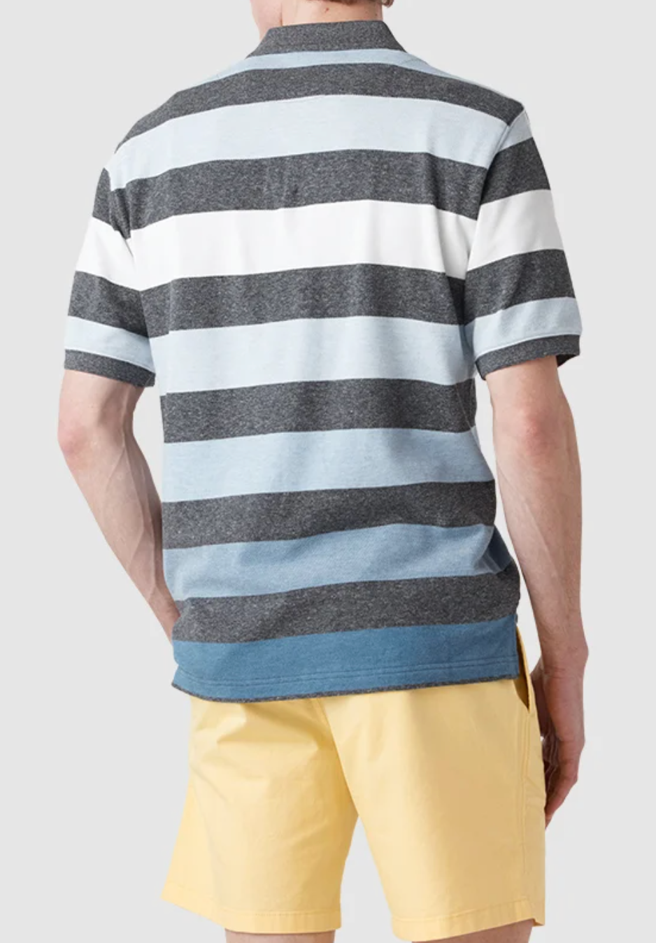 A person wearing a Rodd & Gunn Cox Road Polo in gray, white, and light blue stripes crafted from Australian Cotton is facing away from the camera. The polo features an embroidered logo and is paired with pale yellow shorts.