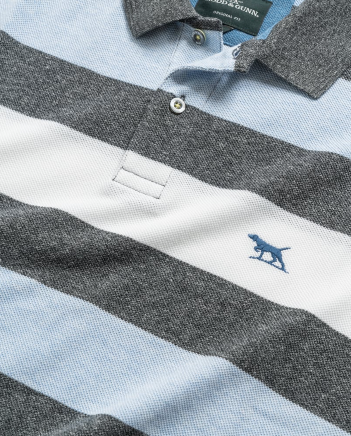 Close-up of a Rodd & Gunn Cox Road Polo in gray and light blue stripes, crafted from soft Australian cotton. It features a small blue embroidered dog logo on the chest, with the collar and button placket adding sophisticated detail to its design.