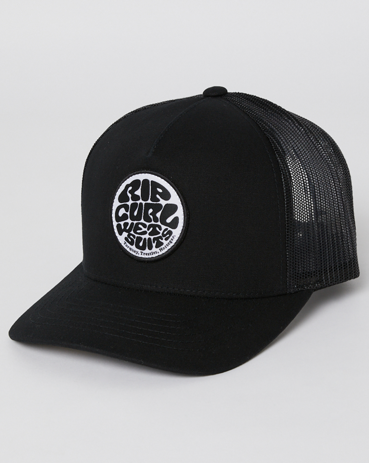 The Rip Curl Icons Eco Trucker cap is black with a round white patch displaying "Rip Curl Wet Suits" in stylized black lettering. Made from recycled polyester twill, it features a mesh back and a slightly curved brim on a plain white background.