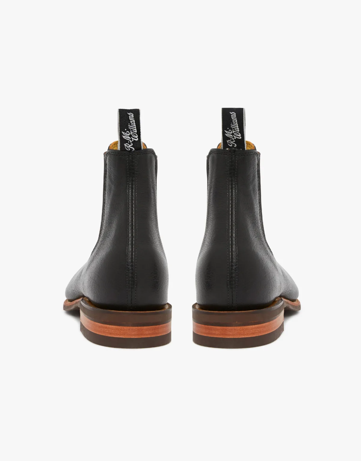 Revised Sentence: Rear view of a pair of RM Williams Comfort Kangaroo Craftsman Boots in black leather with brown soles. The elastic-sided boots feature pull tabs at the back, adorned with white script text. Handcrafted in Australia from premium materials, the image against a white background emphasizes their sleek, polished appearance.