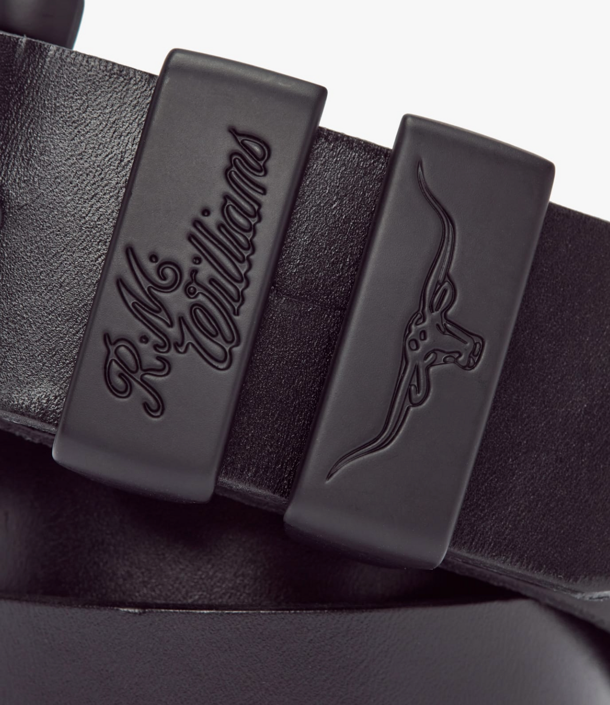 Close-up image of a black RM Williams Drover 1 1/2 Belt featuring a textured, vegetable-tanned leather finish. The belt has two fixed loops: one embossed with the RM Williams logo and the other with a horned bull head design.