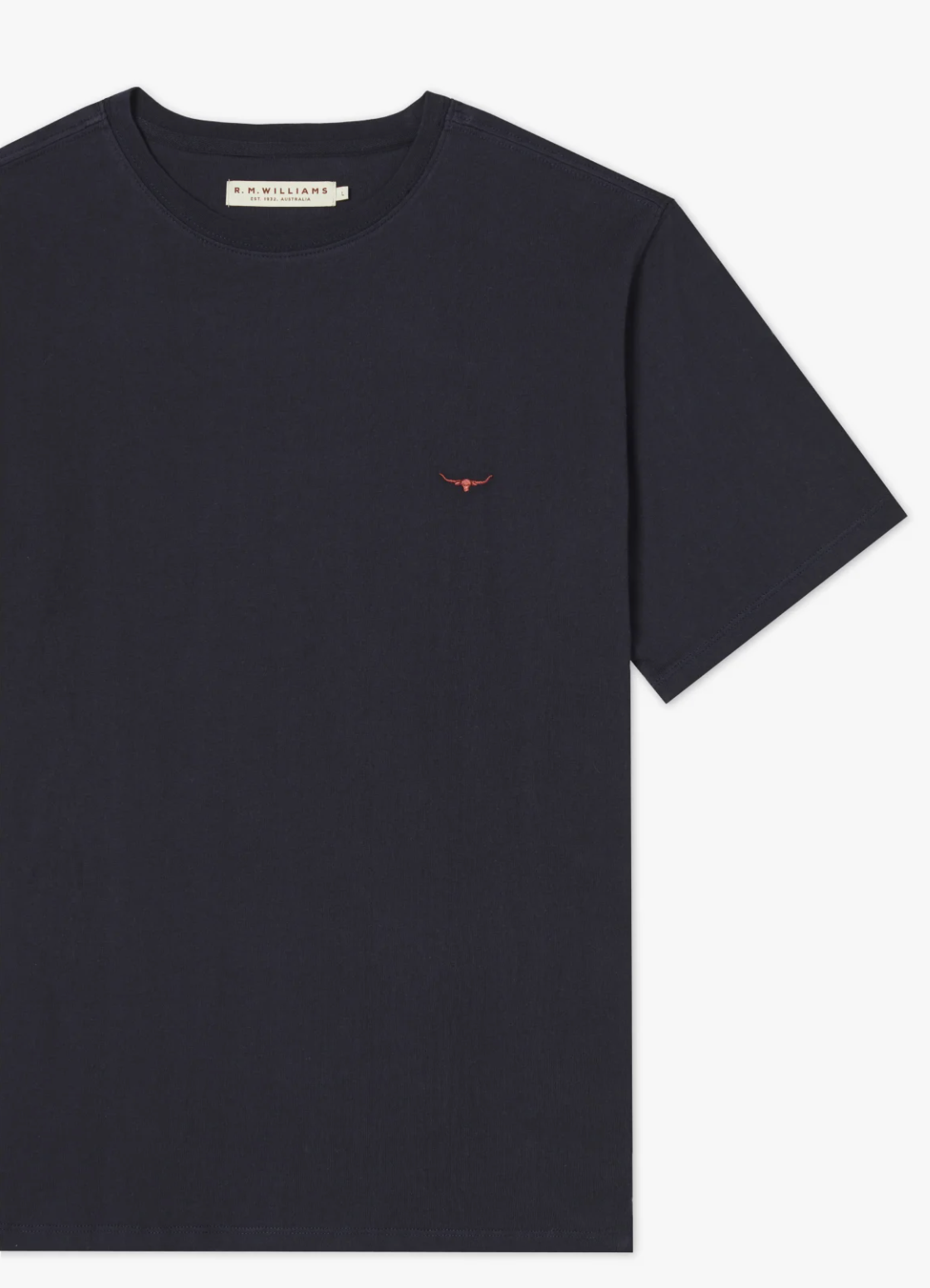 A plain dark blue RM Williams Parson T-Shirt featuring a small, embroidered red logo of bull horns on the left chest. Made from pure cotton jersey, the shirt has a round neckline and short sleeves. An off-white tag with text is visible on the inside collar.