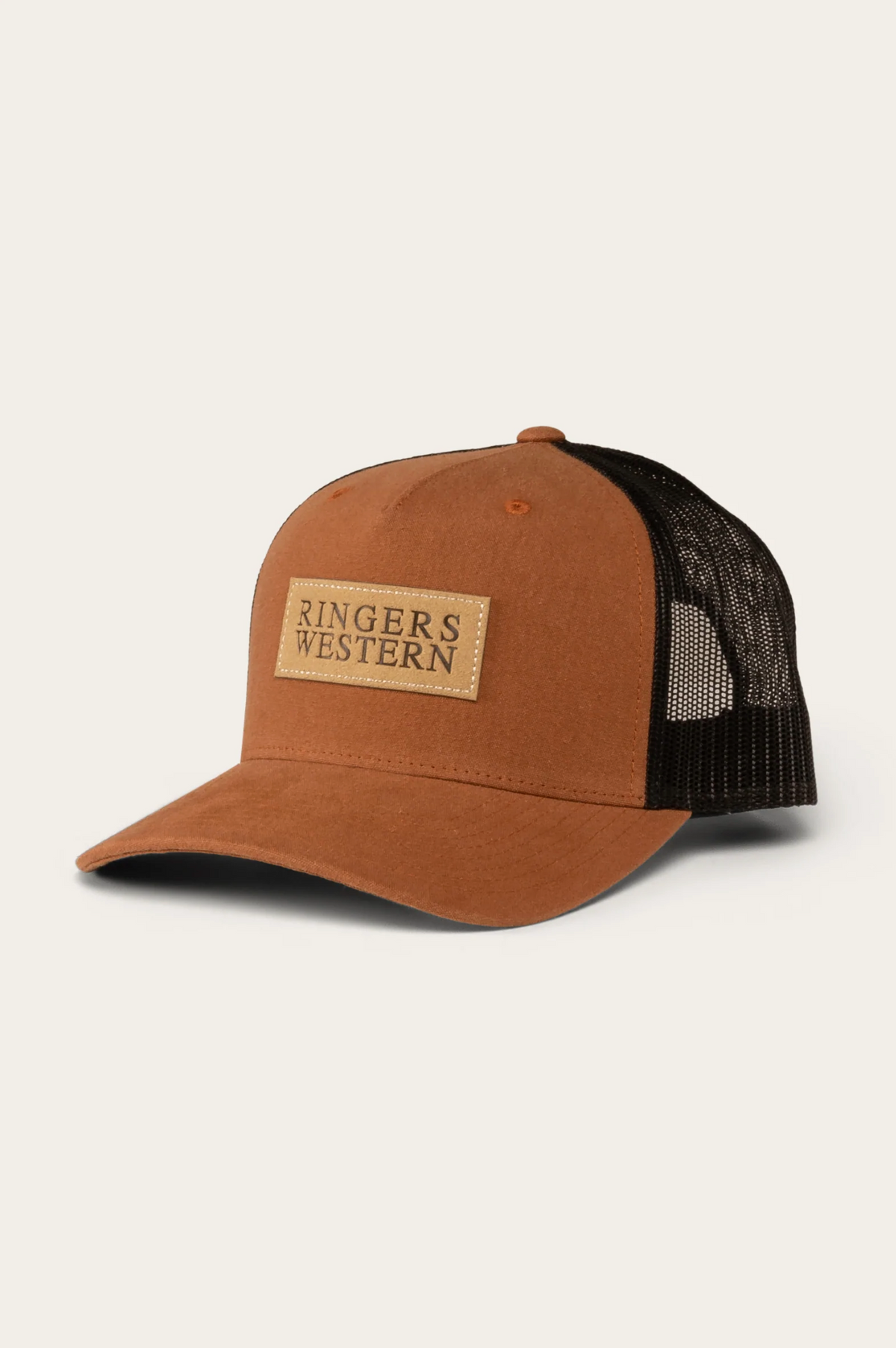 The Ringers Western Dustin Trucker Cap is a brown and black cap made from durable cotton twill with a mesh back. It has a curved brim, structured design, and features a beige rectangular patch on the front panel with "Ringers Western" text, combining style and comfort.
