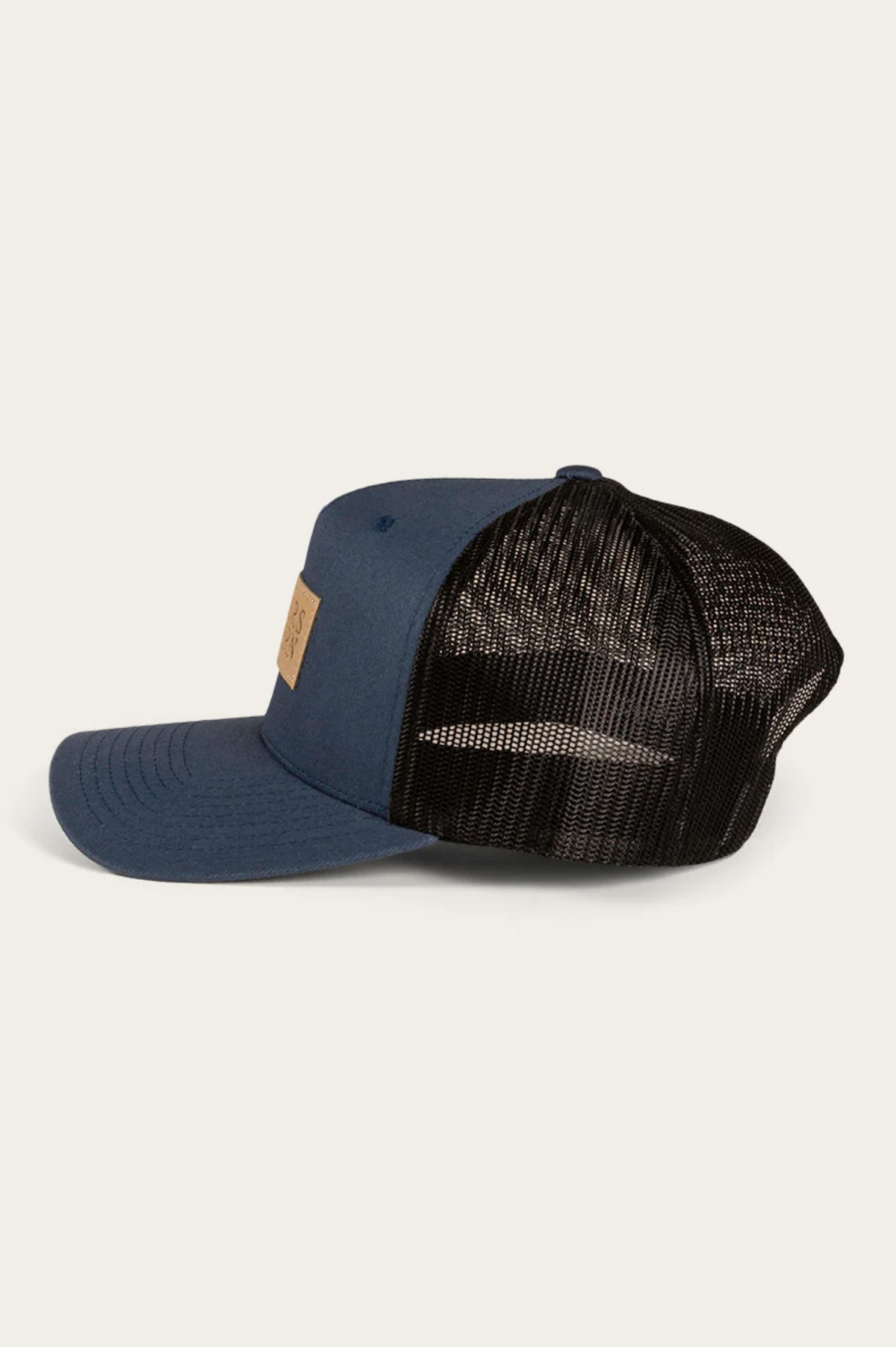 The Ringers Western Dustin Trucker Cap features a blue and black design with a mesh back and a cotton twill brown patch on the front, angled stylishly against a white background.
