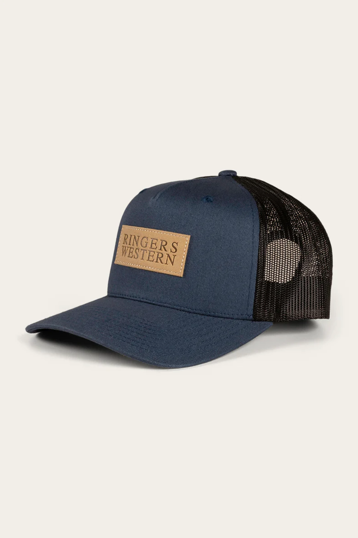 The Ringers Western Dustin Trucker Cap is a navy blue cotton twill hat with a black mesh back and a tan rectangular logo patch reading "RINGERS WESTERN" on the front, angled on a plain background.