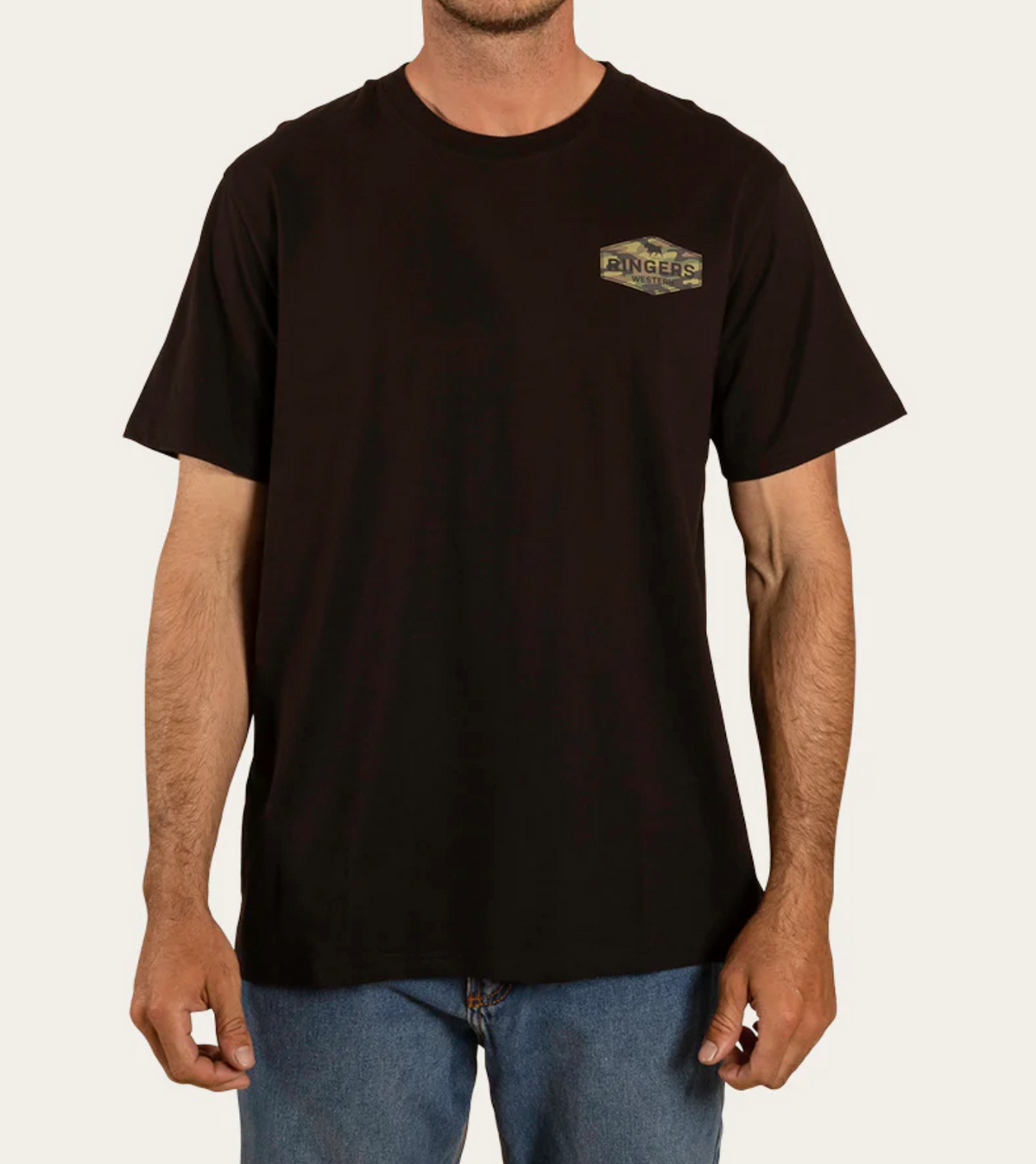 A man in a comfy Ringers Western Servo Loose Fit black T-shirt with a chest graphic stands against a neutral background. Paired with blue jeans, he exudes an effortlessly casual vibe. His head is not visible in the image.