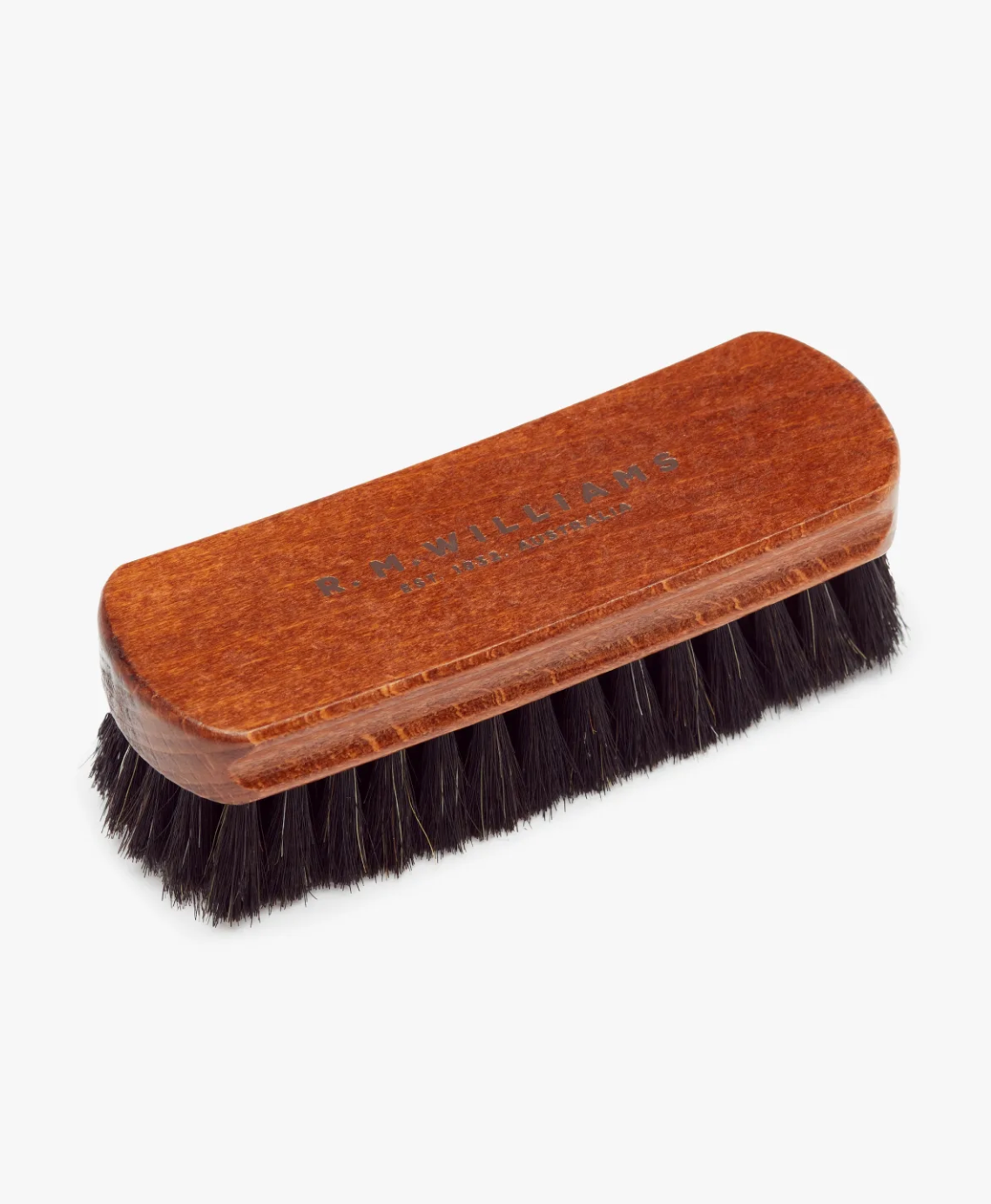 The RM Williams Medium Brush is a rectangular wooden leather boot brush featuring light brown horse hair bristles. The top of the brush is engraved with "R.M. Williams" and "Made in England." The densely packed bristles are ideal for polishing shoes.