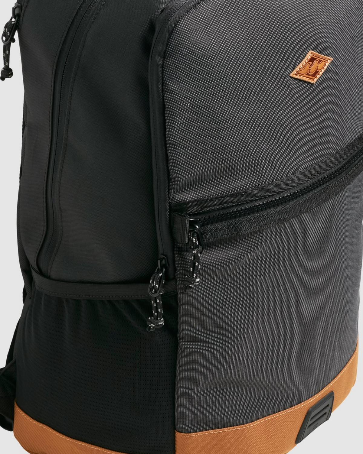 The Billabong Norwest Pack features a gray and black design, accented with a small brown patch on the corner. It includes dual zippers, a brown base, durable material texture, and ergonomic shoulder straps for comfort.