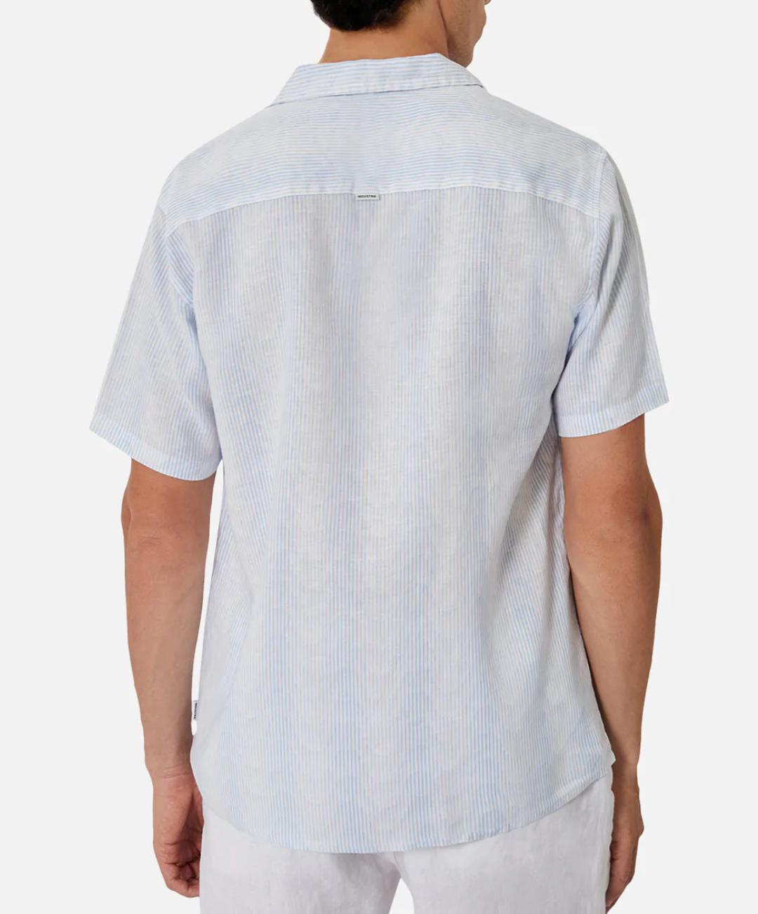 From behind, a person is wearing Industrie The Tropicana Shirt—a light blue and white striped, short-sleeve, button-down shirt with a relaxed fit and collar. Made from 100% linen, it pairs effortlessly with white pants against a plain white background.