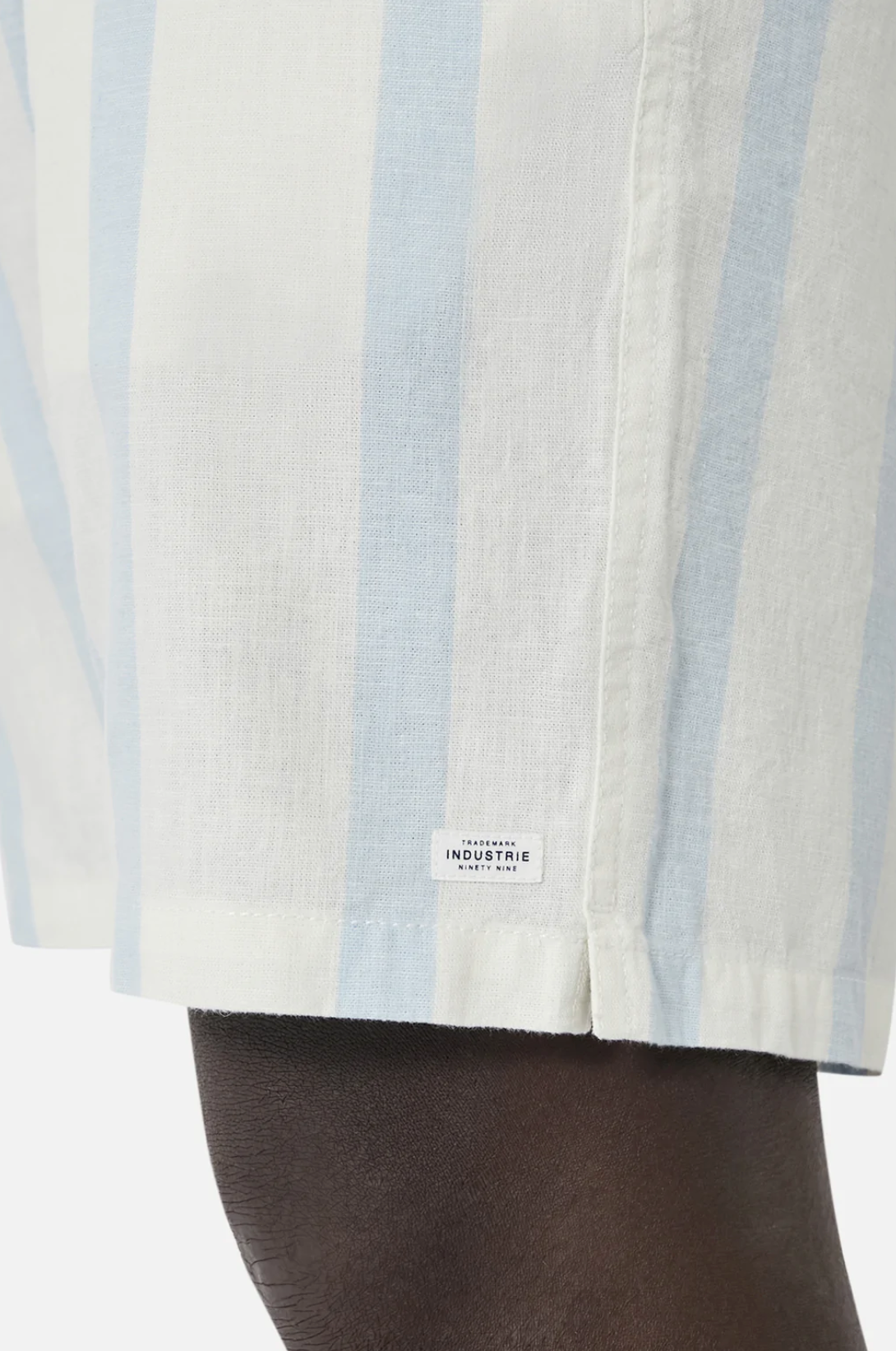 A person wears Industrie The Mykonos Short in light blue and white stripes, showcasing an elasticized waist and an Industrie patch detail against a plain backdrop.