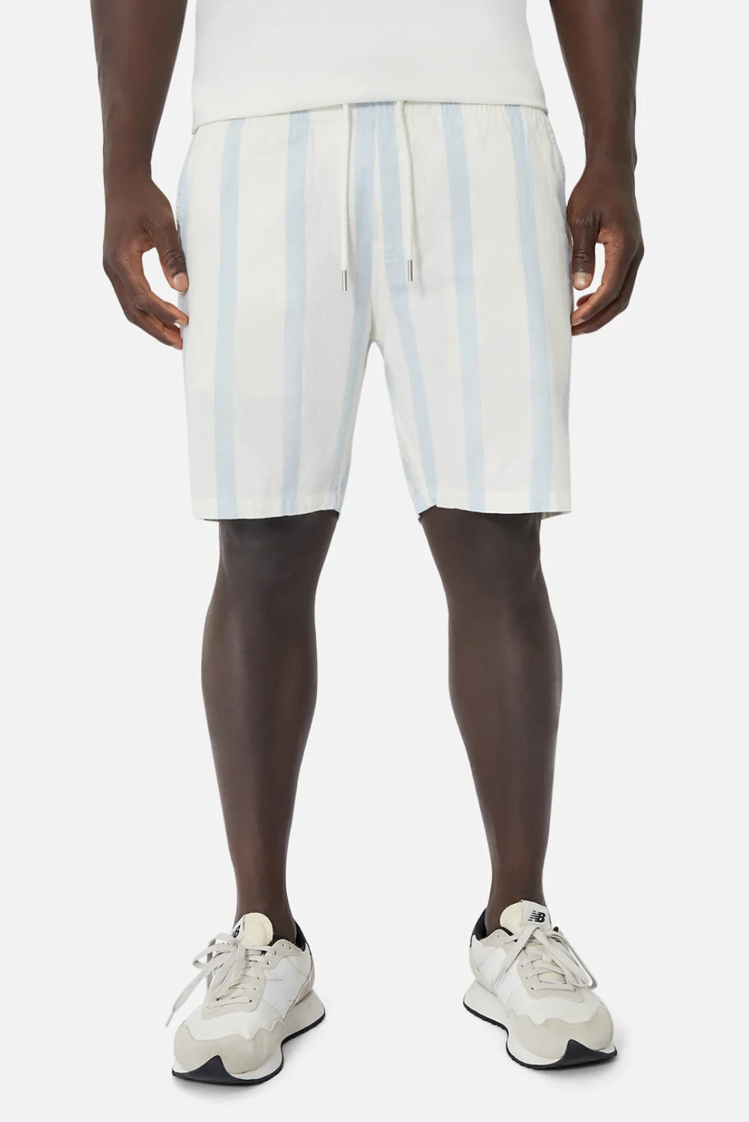 Someone wears the Industrie The Mykonos Short in light blue/white stripes, featuring an elasticised waist and subtle Industrie patches. They're paired with white sneakers with gray accents and shown against a plain white background.