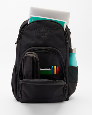 The Billabong Command Backpack, in sleek black recycled polyester, features multiple compartments to hold a laptop, notebooks, a small bag, and colored pens. A teal water bottle fits in its side pocket. It stands upright against a white backdrop, highlighting its stylish laptop compartment.