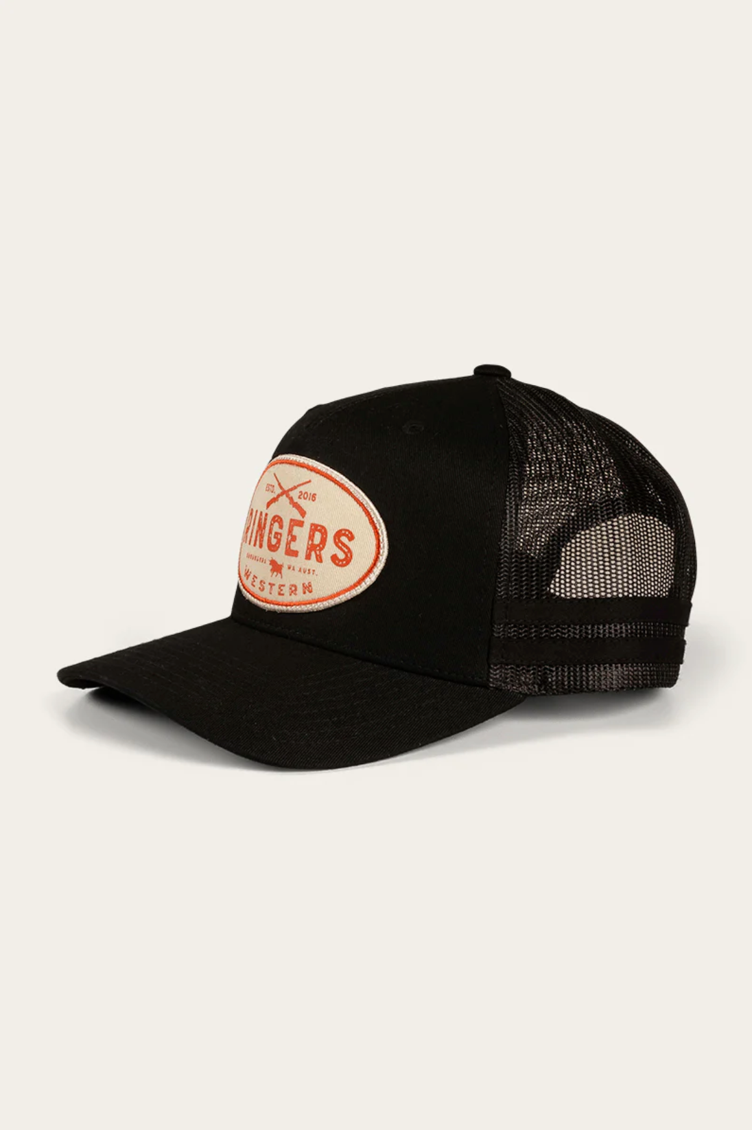 The Ringers Western Deacon Trucker Cap is black with a mesh back and curved brim, made from durable cotton twill. It features a white oval patch with red text and small crossed graphics on the front, capturing the iconic Ringers Western style.