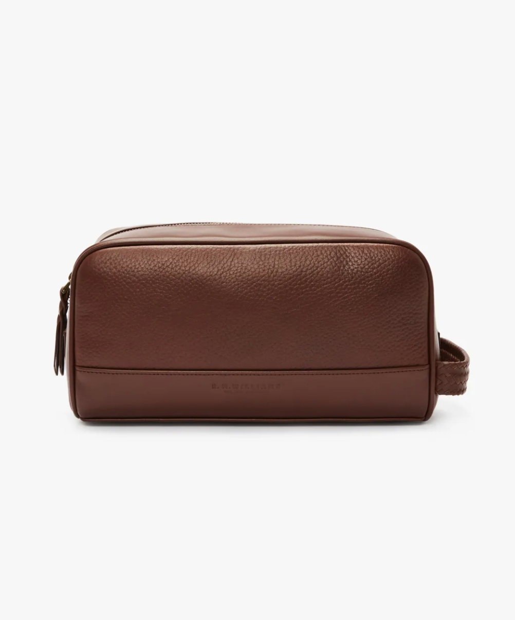 The RM Williams City Washbag is crafted from brown full grain leather and features a zipper closure on top, along with a side handle. This washbag by R.M.Williams boasts a smooth, minimalist design with subtle embossing near the bottom.