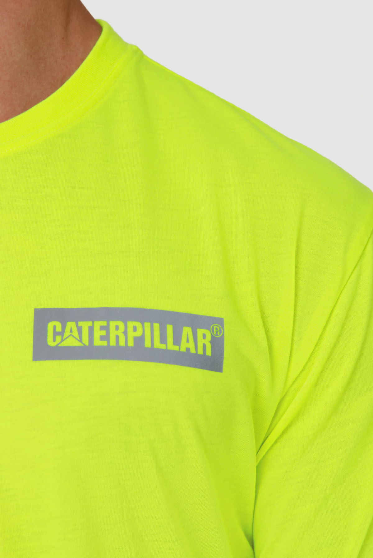 Close-up of a person in a vivid yellow-green CAT Triton Block Tee, crafted from 100% cotton with the gray "Caterpillar" logo on the chest. The fabric is designed for moisture-wicking and is set against a plain white background.
