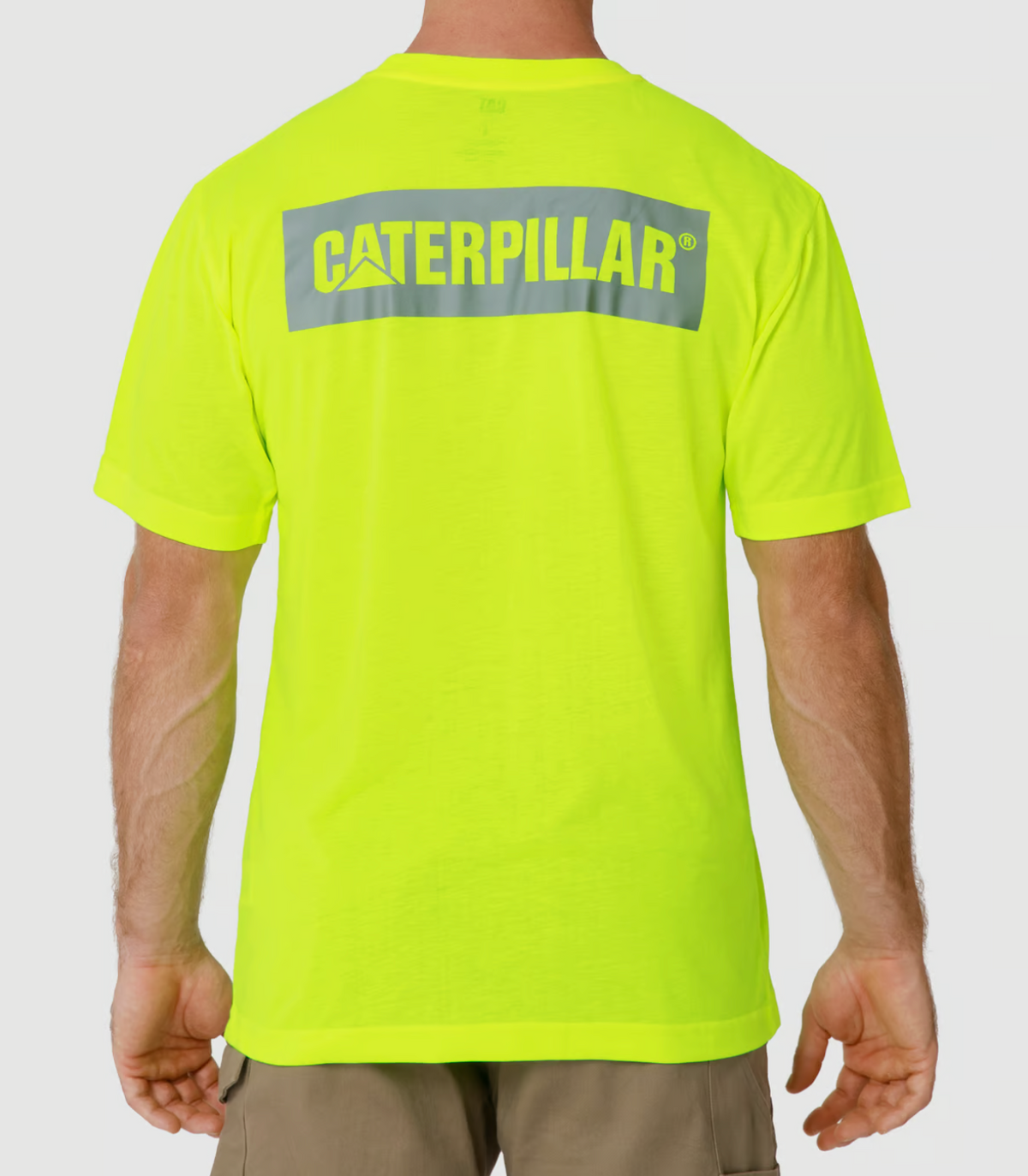 A person is shown from the back wearing a bright yellow CAT Triton Block Tee made of 100% cotton and beige shorts, displaying the gray logo. The tee's moisture-wicking fabric ensures comfort, all set against a plain white backdrop.