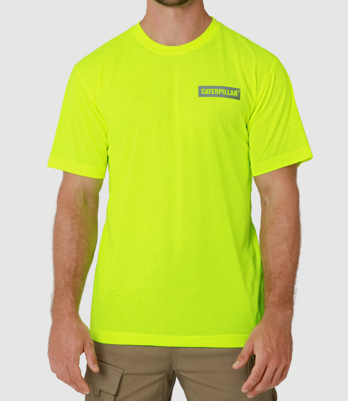 A person is wearing a bright yellow, moisture-wicking CAT Triton Block Tee and brown cargo pants. This 100% cotton T-shirt showcases the Caterpillar logo on the left chest. The background is plain white.