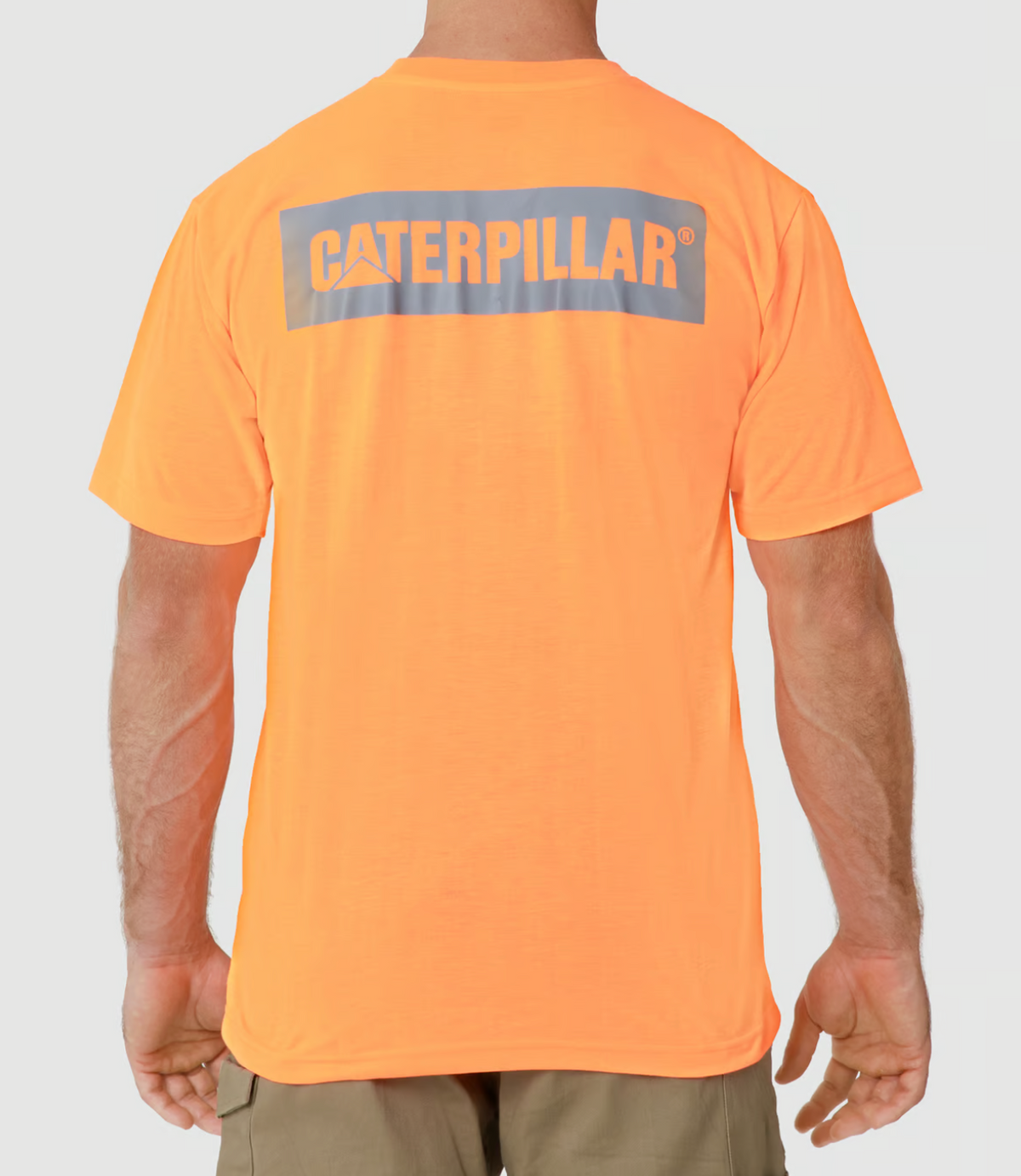 A person is shown from the back wearing the CAT Triton Block Tee, an orange 100% cotton shirt with "Caterpillar" in gray and white letters, highlighting their short hair and muscular arms. They complete the look with beige pants.