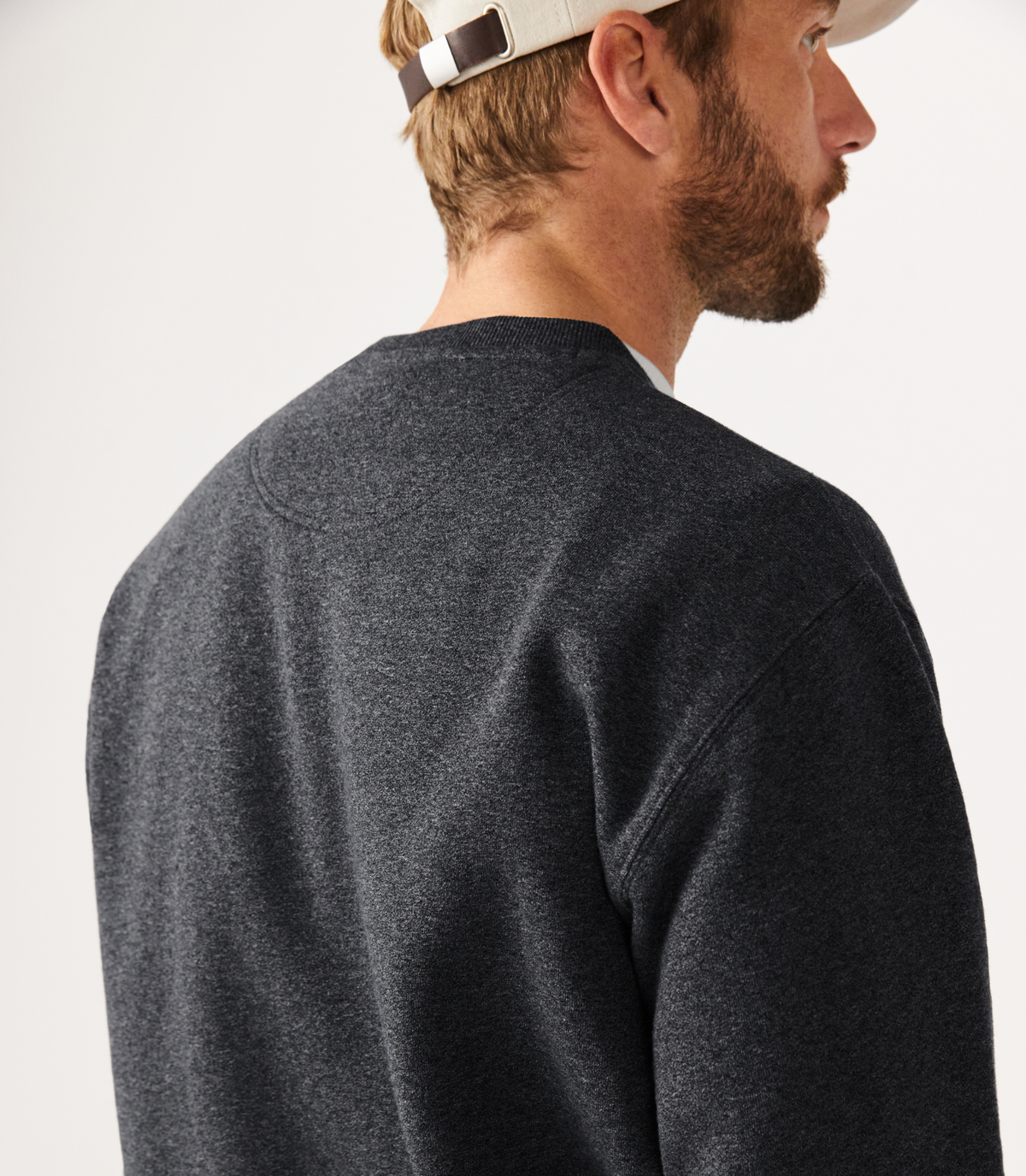 A man in an RM Williams Script Crew Neck and a beige baseball cap faces away from the camera against a light-colored background.