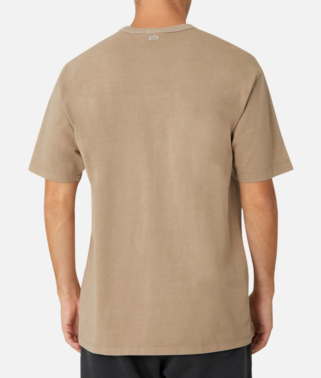 A person is shown from the back wearing Industrie The Del Sur Tee, a plain beige 100% cotton casual T-shirt with an oversized fit for comfort, paired with dark pants. A small tag is visible at the collar, and the backdrop is a plain white.