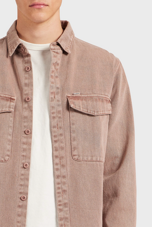 A person wears the Academy Brand Essential Overshirt in dusty pink 100% cotton, styled open over a light beige tee. The overshirt features two chest pockets and is shown from shoulders to mid-torso against a plain background.