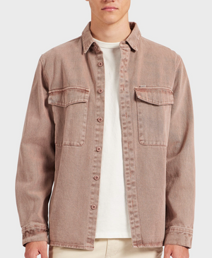 A person wears the Academy Brand Essential Overshirt in light brown 100% cotton with chest pockets, layered over a white t-shirt and beige pants, standing against a plain light background.