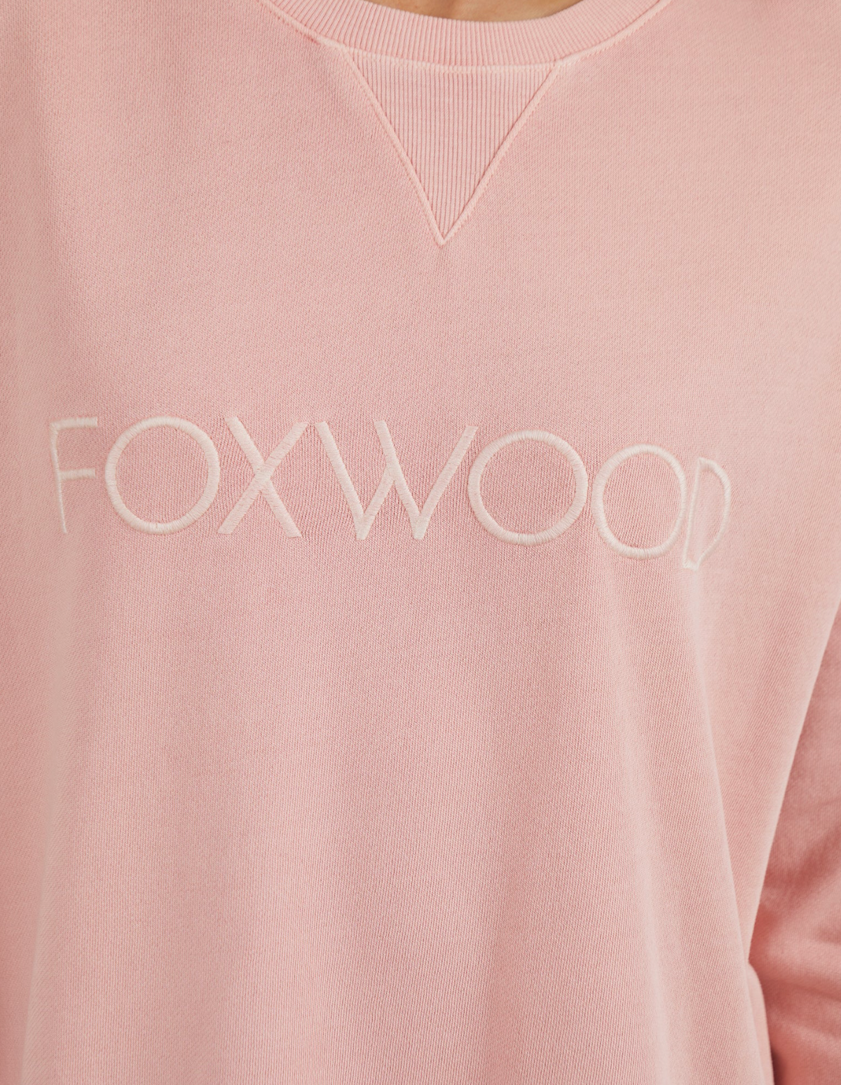 Close-up of the Foxwood Simplified Crew, a pale pink cotton jumper featuring "FOXWOOD" elegantly embroidered in white thread across the chest.