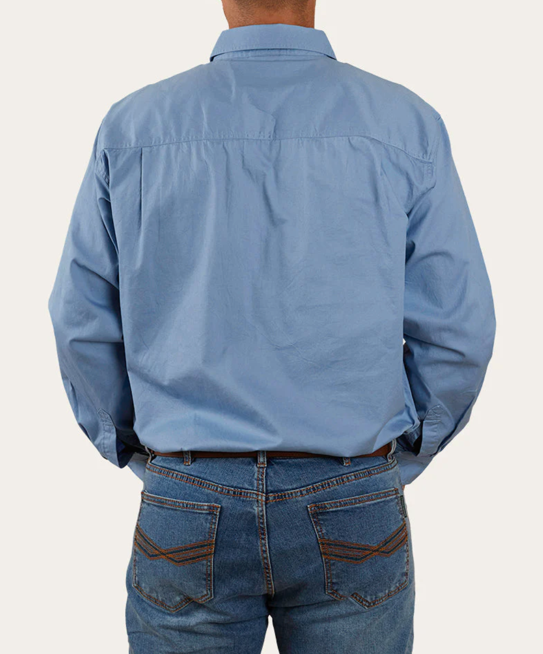 A person stands with their back to the camera, wearing a light blue Ringers Western King River Half Button Shirt made from 100% cotton and blue jeans with distinctive pocket designs. The shirt is untucked against a plain white background.