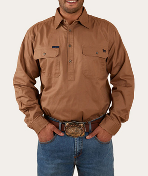 A person wearing the Ringers Western King River Half Button Shirt, a long-sleeved, button-up brown work shirt made from 100% cotton with two chest pockets and featuring a small embroidered animal logo on the left chest pocket, paired with blue jeans. They are also sporting a large, ornate belt buckle and have their hands in their pockets.