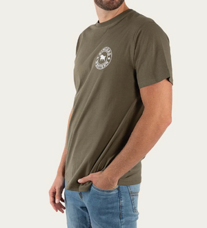 A person wearing a Ringers Western Signature Bull Classic T-Shirt, made from 100% cotton, stands with one hand in their pocket. The green shirt has a chest logo and pairs well with blue jeans against a plain background, with their face unseen.