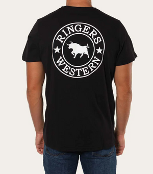 A person is wearing the Ringers Western Signature Bull Classic T-Shirt, a comfortable black tee made of pre-shrunk cotton. The back features a striking white circular logo with a central bull flanked by stars and the words "Ringers Western" encircling it. They pair it with blue jeans and are facing away from the camera.
