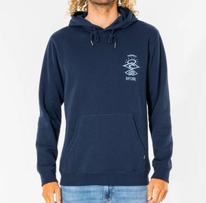 A person in a navy Rip Curl Search Icon Hood with fleece lining, featuring a small graphic and "RIP CURL" text on the chest, paired with light blue jeans. The hoodie has a drawstring and front pocket, set against a plain white background.