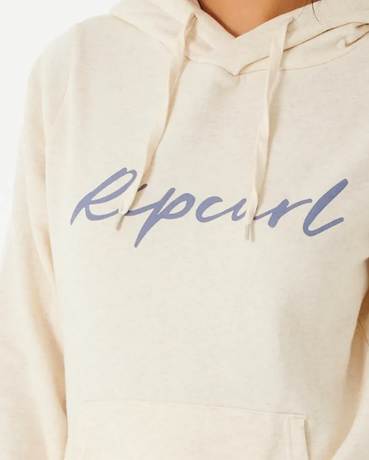 Wearing a cream Rip Curl Script II Hood featuring "Ripcurl" in blue script across the chest, a person dons this cozy casual hoodie with a drawstring hood and fleece lining. Only the upper torso is visible against a white background.