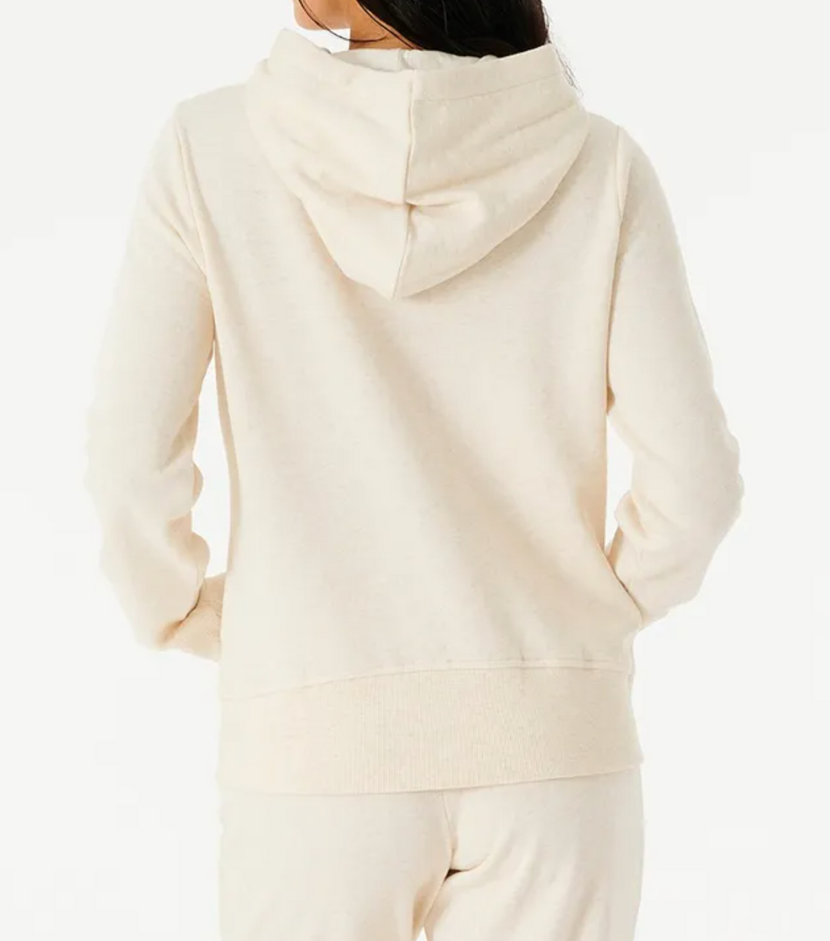 Rear view of a person wearing the cream-colored Rip Curl Script II Hood with matching pants. The soft fleece lining hoodie drapes its hood gracefully over their back, and the plain white background enhances the cozy look.
