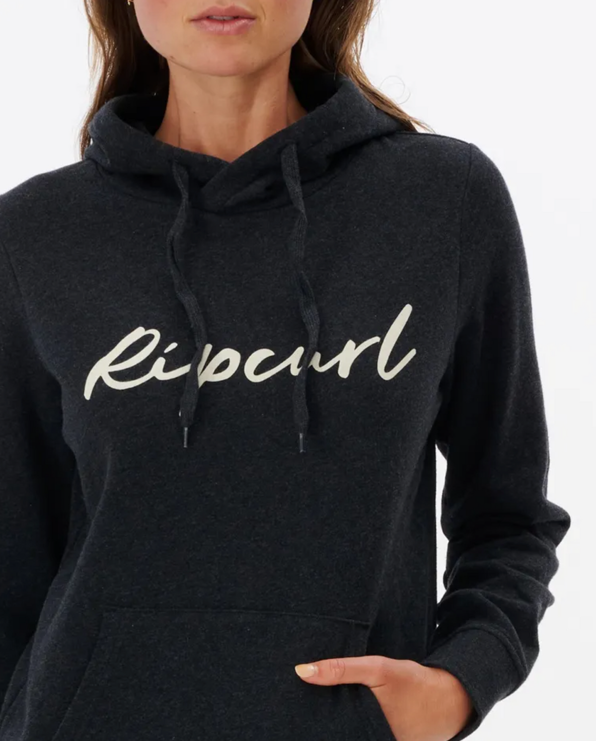 Someone is wearing the Rip Curl Script II Hood, which stylishly displays the brand name in cursive on the front, with one hand casually resting in its fleece-lined pocket against a plain white background.