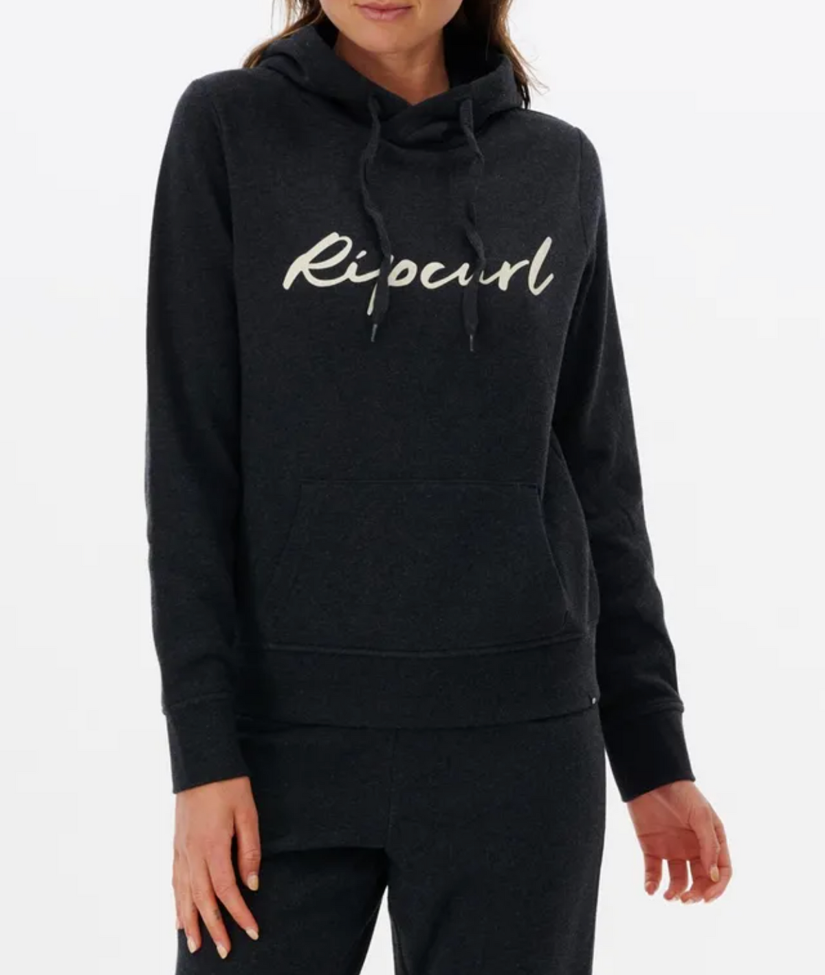 A person wears a dark Rip Curl Script II Hood, showcasing "Ripcurl" in white text. This casual hoodie has a front pocket, drawstrings at the neckline, and cozy fleece lining as they stand against a plain background.