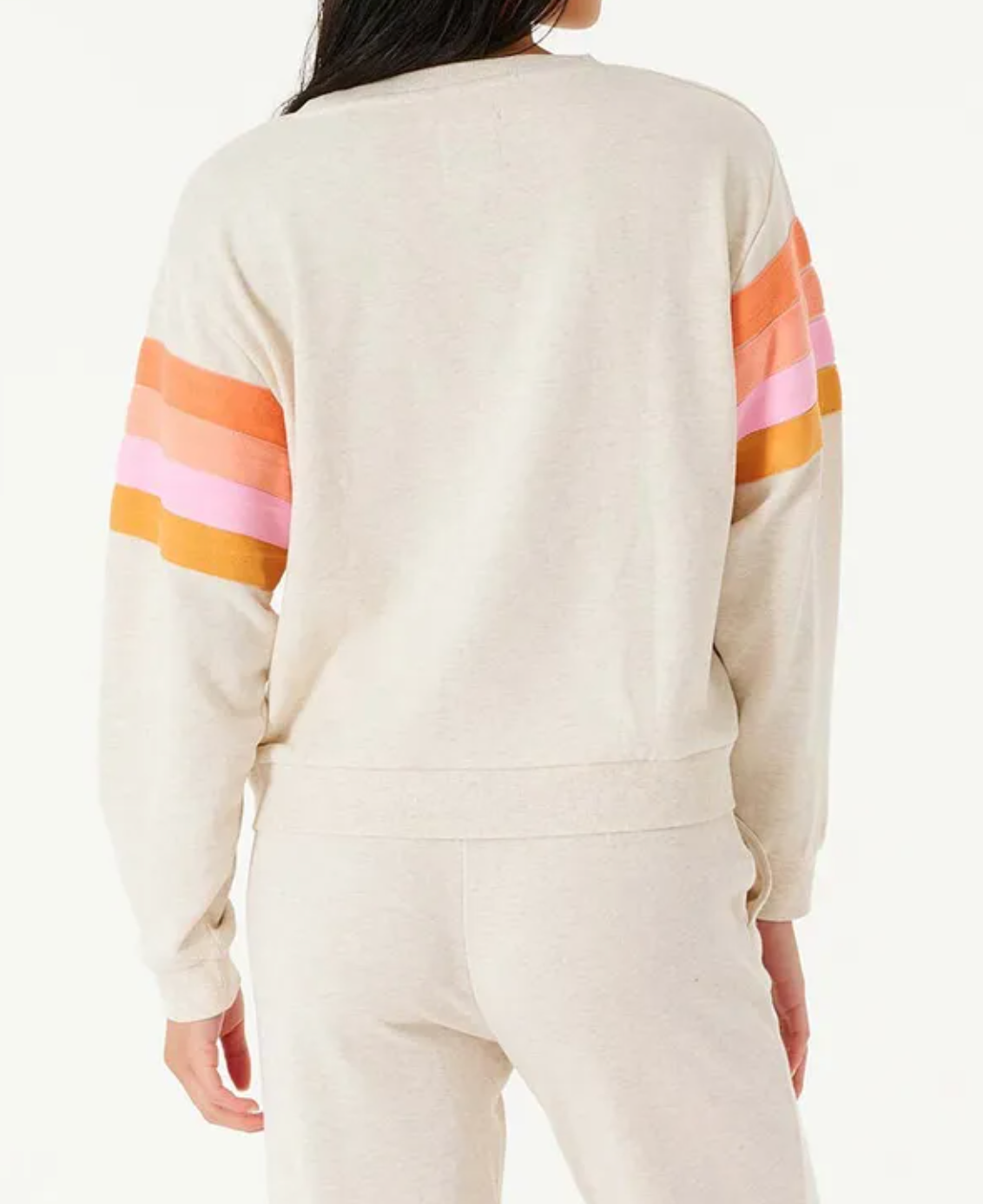 A person seen from behind is wearing a Rip Curl Day Break Crew sweatshirt, cream-colored with horizontal orange and pink sleeve stripes, paired with matching cream sweatpants. The crew offers a relaxed fit against a plain white background.
