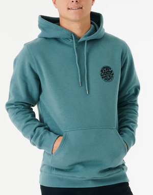 Against a white background, someone wears a Rip Curl Wetsuit Icon Hood. This comfy hoodie is crafted from organic cotton, showcasing a teal design with a black circular "RIP CURL BOARD SHORTS" logo on the left chest, complete with drawstrings and a front pocket.