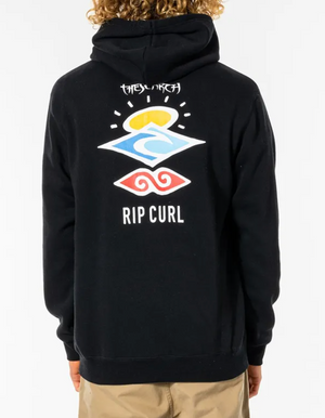 Back view of a person with curly blonde hair wearing the Rip Curl Search Icon Hood, a comfortable black casual hoodie. The hoodie, made from soft fleece lining and Organic Brushed Cotton, features a colorful wave design along with the words "THE SEARCH" and "RIP CURL" printed on the back. The person is also wearing beige pants.
