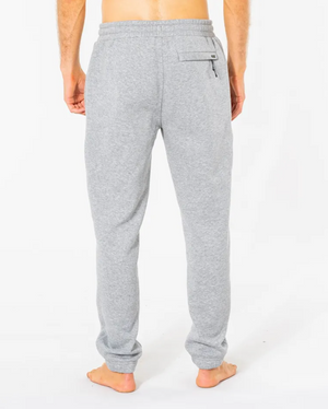 A person is seen barefoot from behind against a white background, wearing light gray Rip Curl Search Icon Track Pants. These comfy pants are crafted from organic brushed cotton and feature an elastic waistband with a back right pocket.