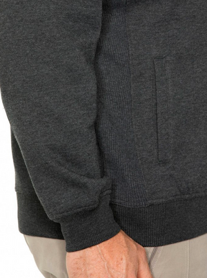 A close-up of a person's hand by their side, casually dressed in dark gray Breakaway Zed Snowy Mt Fleece Full Zip with ribbed texture and cuffed sleeves, paired with light-colored pants. The fleece features a concealed pocket.