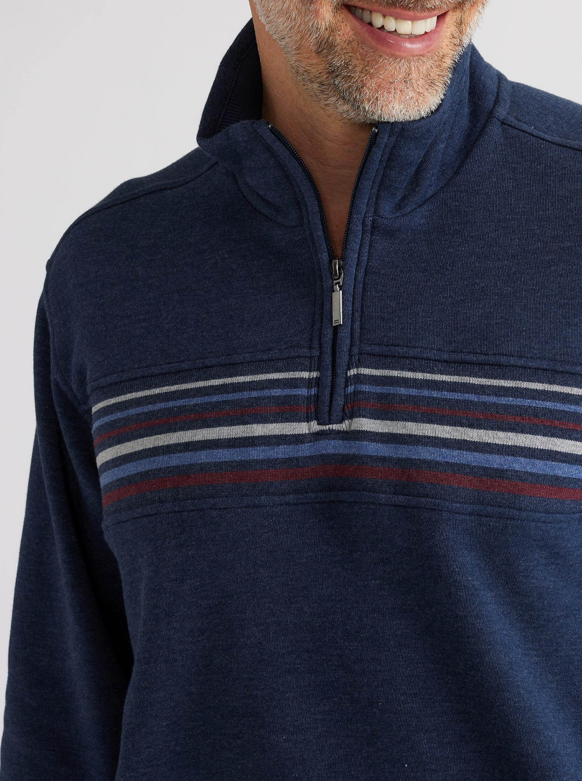 A smiling man with a short beard wears the Breakaway Huxter Snowy Mt Fleece 1/2 Zip, a casual navy sweater with horizontal gray, blue, and red stripes across the chest. Only his lower face and upper torso are shown.